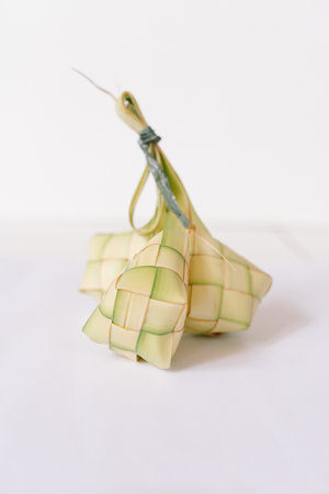 Ketupat, traditional rice dumpling served during Eid al-Fitr. Cooked rice is packed inside a diamond-shaped container of woven palm leaf pouch. Isolated on white background.の写真素材