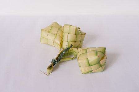 A trio of ketupat, traditional rice dumplings, sits on a plain white surface. These iconic woven packets, crafted from young coconut leaves, are an essential culinary feature of Eid and other Southeast Asian festivities, symbolizing both tradition and celebration.の写真素材