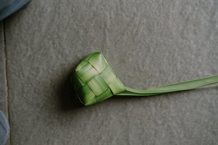 A hand-crafted ketupat, a traditional rice dumpling, sits ready for cooking. This woven palm leaf pouch, filled with rice, is a cherished festive food during Eid al-Fitr in Indonesia and Southeast Asia. Its intricate design and natural green hue showcase a cultural culinary art.の写真素材