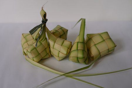 Ketupat are rice dumplings popular during Eid al-Fitr. Woven from coconut leaves and filled with rice, these savory treats are a staple in Southeast Asian celebrations. Photographed on a white background, their unique shape and festive appearance represent a symbol of culture and tradition.の写真素材