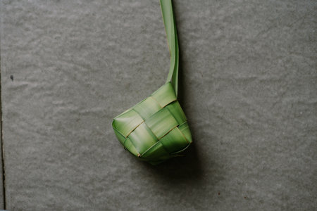A meticulously woven ketupat made from palm leaves, symbolizing tradition and culinary heritage. Perfect for showcasing Southeast Asian culture, festive occasions like Eid, or the art of food presentation. The intricate weave design adds depth and texture.の写真素材