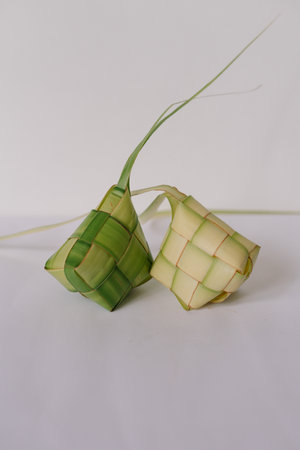 Studio shot of Ketupat, a traditional rice dumpling packed inside a diamond-shaped container of woven palm leaf pouch, on a white surface. It's a festive dish during special occasions. Can be used as graphic resource.の写真素材