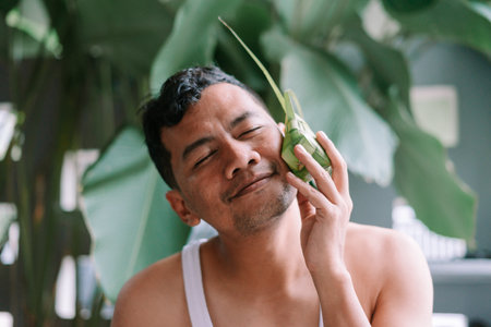 A contented man with closed eyes gently touches his face with a ketupat, showcasing the beauty and significance of this traditional food. The image captures the serene ambiance of the Eid al-Fitr celebration, resonating with cultural richness.の写真素材