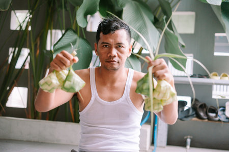 An indonesian man holds aloft ketupat, a traditional rice dumpling made from woven palm leaves, during the festive Eid al-Fitr celebration. A culinary delicacy enjoyed during Ramadan and other special occasions.の写真素材
