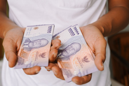 Close up of Indonesian Rupiah cash money being held by a person. The 10,000 Rupiah banknotes are displayed in the hands, showcasing currency and financial concepts.の写真素材