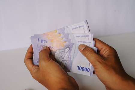 Close-up of hands holding Indonesian Rupiah banknotes. Focus on the hands and the 10000 IDR currency, showcasing financial transactions and wealth. Suitable for illustrating concepts related to economy, investment, and the Indonesian financial market.の写真素材