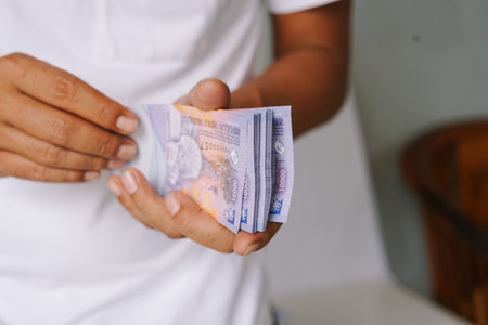 A person holding a stack of indonesian rupiah banknotes. Close-up shot of the currency in hand, representing wealth, finance, savings, and the indonesian economy.の写真素材