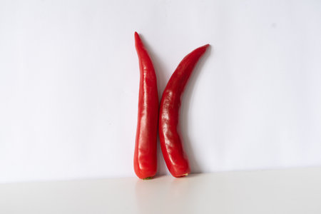 Two minimalist red chili peppers are arranged against a white background, forming a stylized letter 'K'. A spicy and vibrant culinary composition, conveying freshness, heat, and organic ingredients.の写真素材