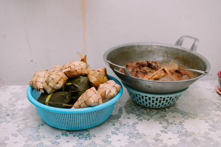 A vibrant presentation of traditional Indonesian dishes, ketupat and rendang, prepared for a festive celebration. The woven palm leaf packets hold flavorful rice, while the savory meat dish simmered in coconut milk and spices adds a rich aroma.の写真素材