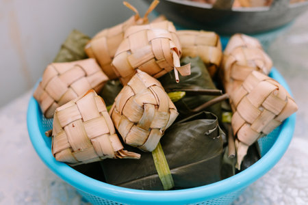 Close-up shot of Ketupat and Lepet in a blue basket. Both are traditional dishes, often served during Eid al-Fitr. Ketupat is a rice dumpling cooked in a woven palm leaf pouch, while Lepet is made from glutinous rice mixed with coconut milk, wrapped in banana leaves.の写真素材