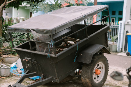 A heavily used utility trailer sits outdoors. The trailer shows signs of wear, suggesting frequent use for hauling equipment, gardening supplies, or other materials. The suburban background adds context to its practical applications.の写真素材