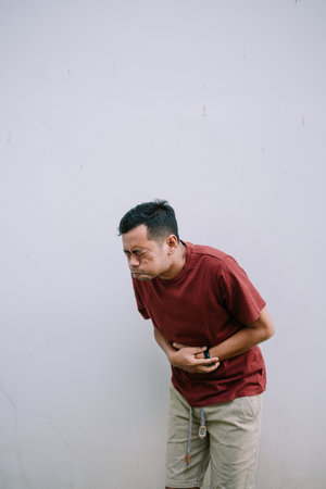 Man suffering from stomach pain. He is holding his abdomen with both hands with a pain expression.の写真素材