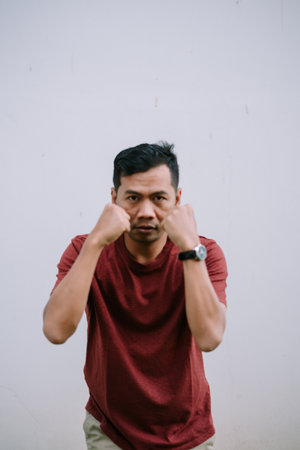 Portrait of a serious asian man with fists up in a defensive pose against a plain backgroundの写真素材