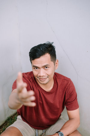 Cheerful man extends his hand in a welcoming gesture, posing against a plain wall. Casual, attractive and friendly.の写真素材