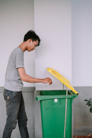 Young man putting trash into green recycling bin. Daily activity for waste management and environmental responsibility.の写真素材