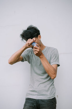 A young man struggles to open a water bottle on a neutral background, showing the everyday...