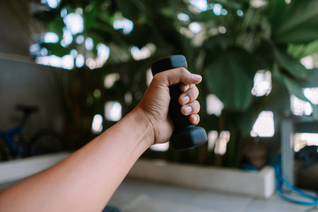 Hand holding a dumbbell. Active lifestyle and exercise for fitness indoors. Strong man training with a weight. Concept of healthy habits.の写真素材