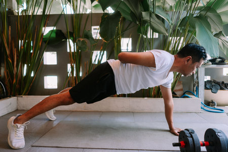 Asian man doing push-ups at home for his fitness routine. Indoor workout with tropical plants as a...