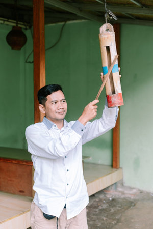 An Indonesian man is playing a bamboo slit drum kentongan using a mallet. Traditional music instrument from java.の写真素材