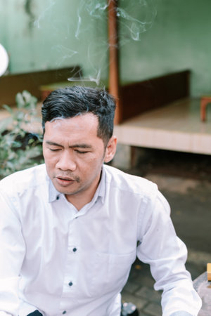 A contemplative man, cigarette smoke rising, lost in thought outdoors.の写真素材