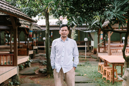 Adult man stands confidently in a traditionally designed Indonesian restaurant. Calm and serene outdoor location.の写真素材