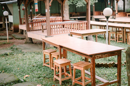 Quiet outdoor setting featuring wooden tables and stools. Perfect for relaxing and enjoying the peaceful atmosphere in this natural environment.の写真素材