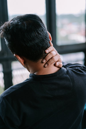 A man massages his neck due to pain. Rear view showing discomfort from muscle tension or injuryの写真素材