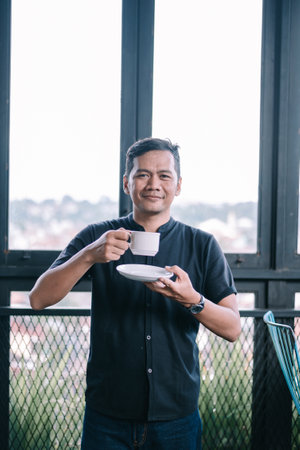 Portrait of a relaxed man with a cup of tea, enjoying a peaceful moment with a city view.の写真素材