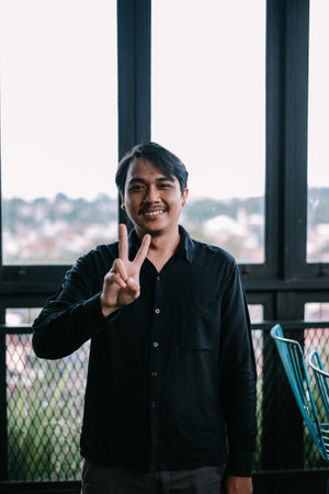 Smiling guy making a peace gesture with a city view backdrop. Shows a positive, happy attitude.の写真素材