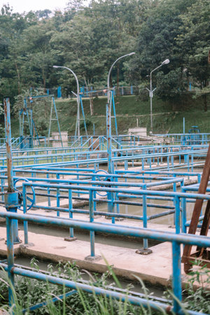 View of a water treatment facility with its intricate blue metalwork against a lush green backdrop. An image representing vital infrastructure, environmental care and public service.の写真素材