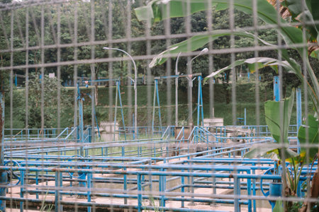 View of a blue painted wastewater treatment facility seen through a security wire fence....