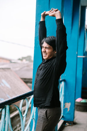 Man stretching outside, on a blue painted balcony, expressing effortの写真素材