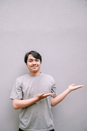 Smiling asian man presenting empty space against grey textured backdrop. Room for your text or graphics.の写真素材