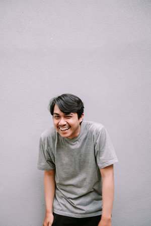 Portrait of a joyful Asian man with a genuine laugh, expressing happiness. Casual wear and a plain backdrop emphasize the candid, carefree mood.の写真素材