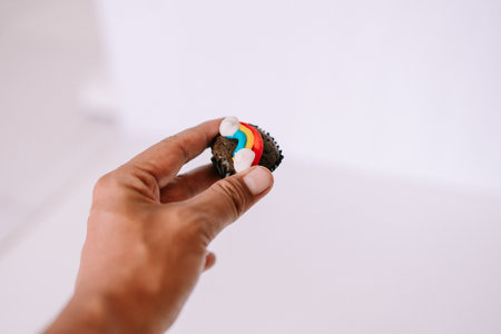 A person is holding a brownie bite decorated with a rainbow frosting detail. A simple and minimal shot on white backgroundの写真素材