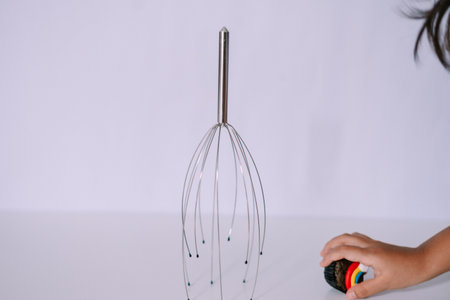 A child's hand reaches for a toy near a head massager, showcasing a playful and therapeutic scenario on a clean, white surface.の写真素材