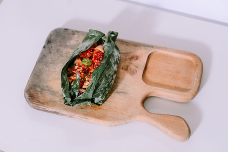 Nasi Bakar wrapped in banana leaf on a rustic wooden tray. Authentic Indonesian grilled rice dish.の写真素材