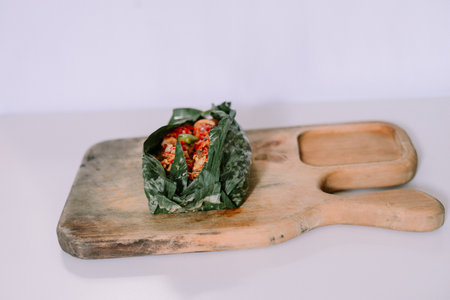 Indonesian pepes tahu, tofu dish seasoned with spices, wrapped in banana leaf. Served on vintage wooden platter.の写真素材