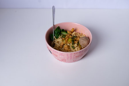 A tasty chicken noodle bowl with fresh vegetables on a plain background is ready to eatの写真素材