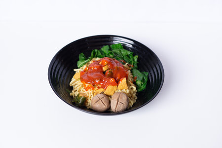 Delicious mie ayam noodle soup with meatball, chicken, and vegetables in a black bowl isolated on whiteの写真素材