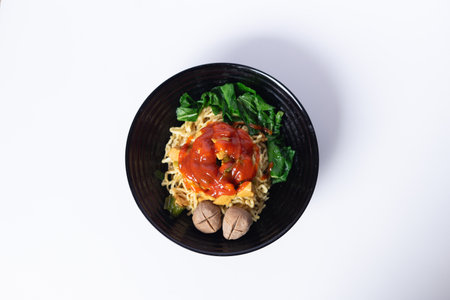 A bowl of tasty asian noodles with vegetables and meatballs, garnished with savory sauceの写真素材