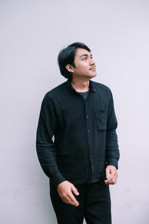 A thoughtful young man in solid black casual wear looks up, lost in thought against a clean white backdropの写真素材