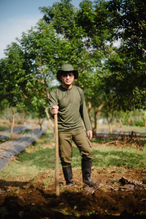 A peanut farmer manually creating holes in the soil using a wooden stick to plant peanut seeds. Traditional farming methodの写真素材