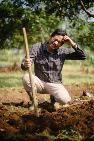 A peanut farmer manually creating holes in the soil using a wooden stick to plant peanut seeds. Traditional farming methodの写真素材