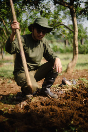 A peanut farmer manually creating holes in the soil using a wooden stick to plant peanut seeds. Traditional farming methodの写真素材