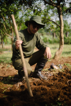 A peanut farmer manually creating holes in the soil using a wooden stick to plant peanut seeds. Traditional farming methodの写真素材