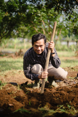 A peanut farmer manually creating holes in the soil using a wooden stick to plant peanut seeds. Traditional farming methodの写真素材