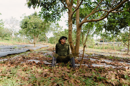 A tired farmer resting under a tree beside his hoe after working in the field. Taking a break from manual labor under the sunの写真素材