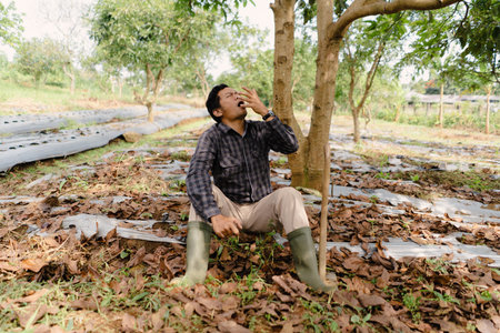 A tired farmer resting under a tree beside his hoe after working in the field. Taking a break from manual labor under the sunの写真素材