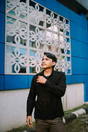 A thoughtful young man contemplating his future, standing outside a modern building with elegant floral design elements.の写真素材